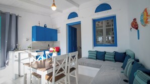 Una cocina moderna con armarios azules, una mesa de comedor con sillas y un espacio de sala acogedor con un sofá y cojines.