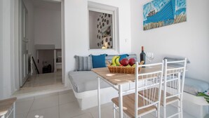Una sala de estar moderna con una mesa de madera, sillas blancas, un sofá con cojines azules y un cuadro de un velero.