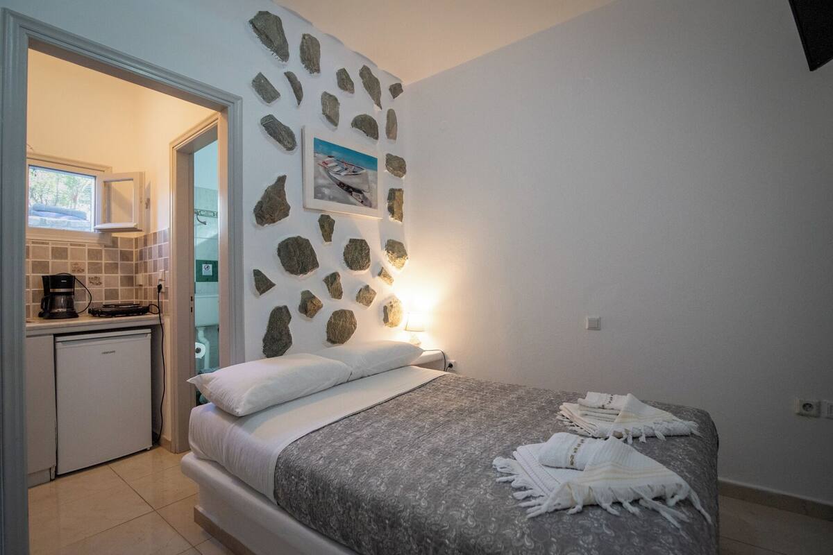 Une chambre avec un lit, un petit coin cuisine et un mur en pierre orné d’un tableau.