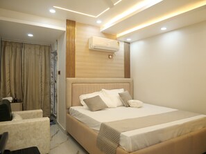 A modern bedroom with a large bed, a bedside table, an air conditioning unit, and a view of a bathroom with a shower and curtains. - Happy Residency (Patna)