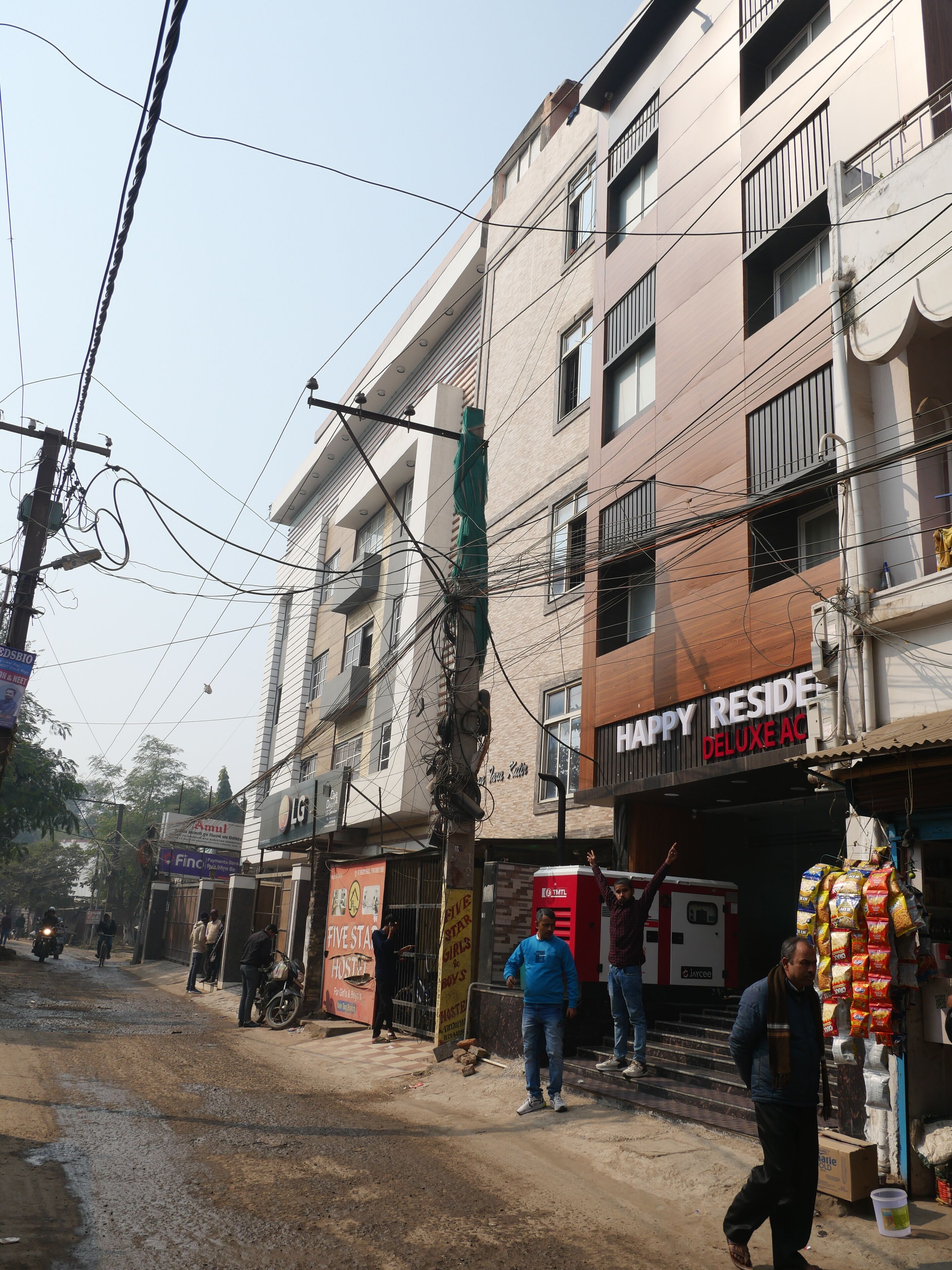 Un edificio de varios pisos con varias tiendas en la planta baja, incluyendo un cartel visible que dice 'Happy Residence Deluxe AC'.