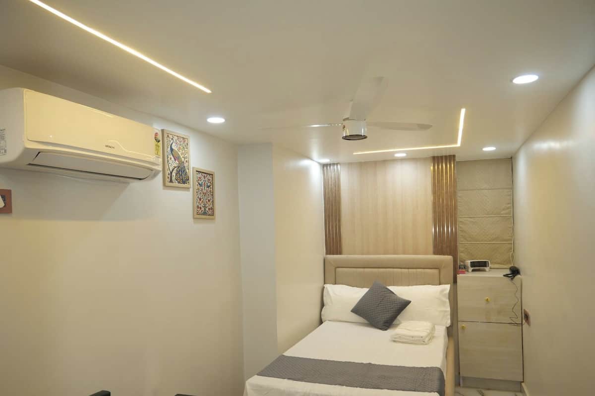 Habitación de hotel con cama, mesita de noche, aire acondicionado, ventilador de techo, obra de arte y ventana con cortinas.