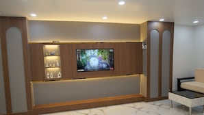 Un soggiorno moderno con una televisione a schermo piatto montata su una parete in legno, un pavimento effetto marmo e una zona salotto con divano.