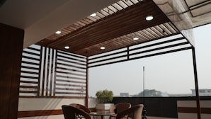Un balcone con soffitto in legno, due sedie in vimini, un tavolino e una pianta in vaso.