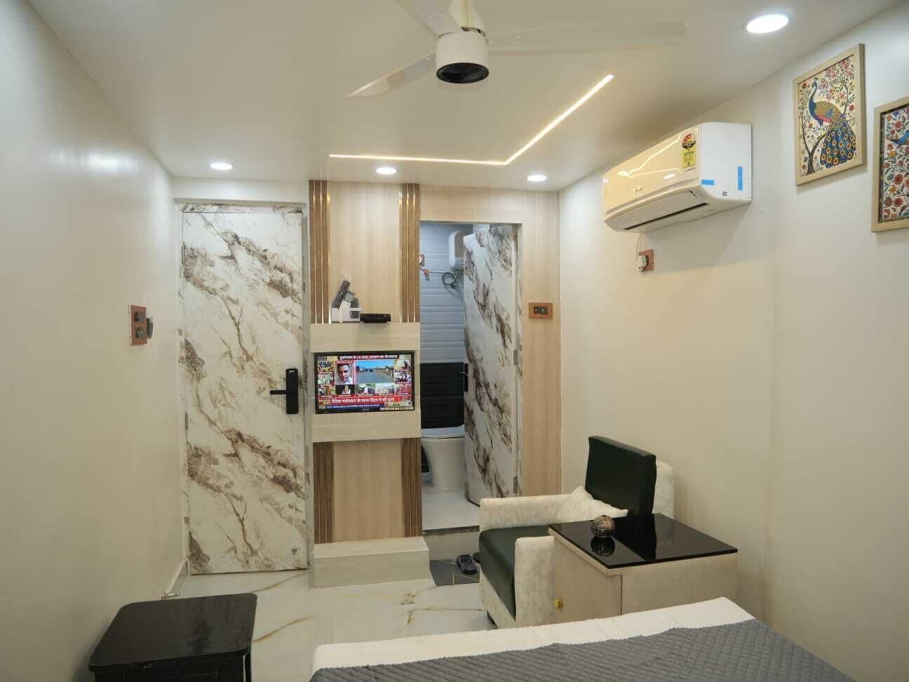 Quarto de hotel pequeno com uma cama, uma mesa com um computador, uma TV na parede e um ar condicionado.
