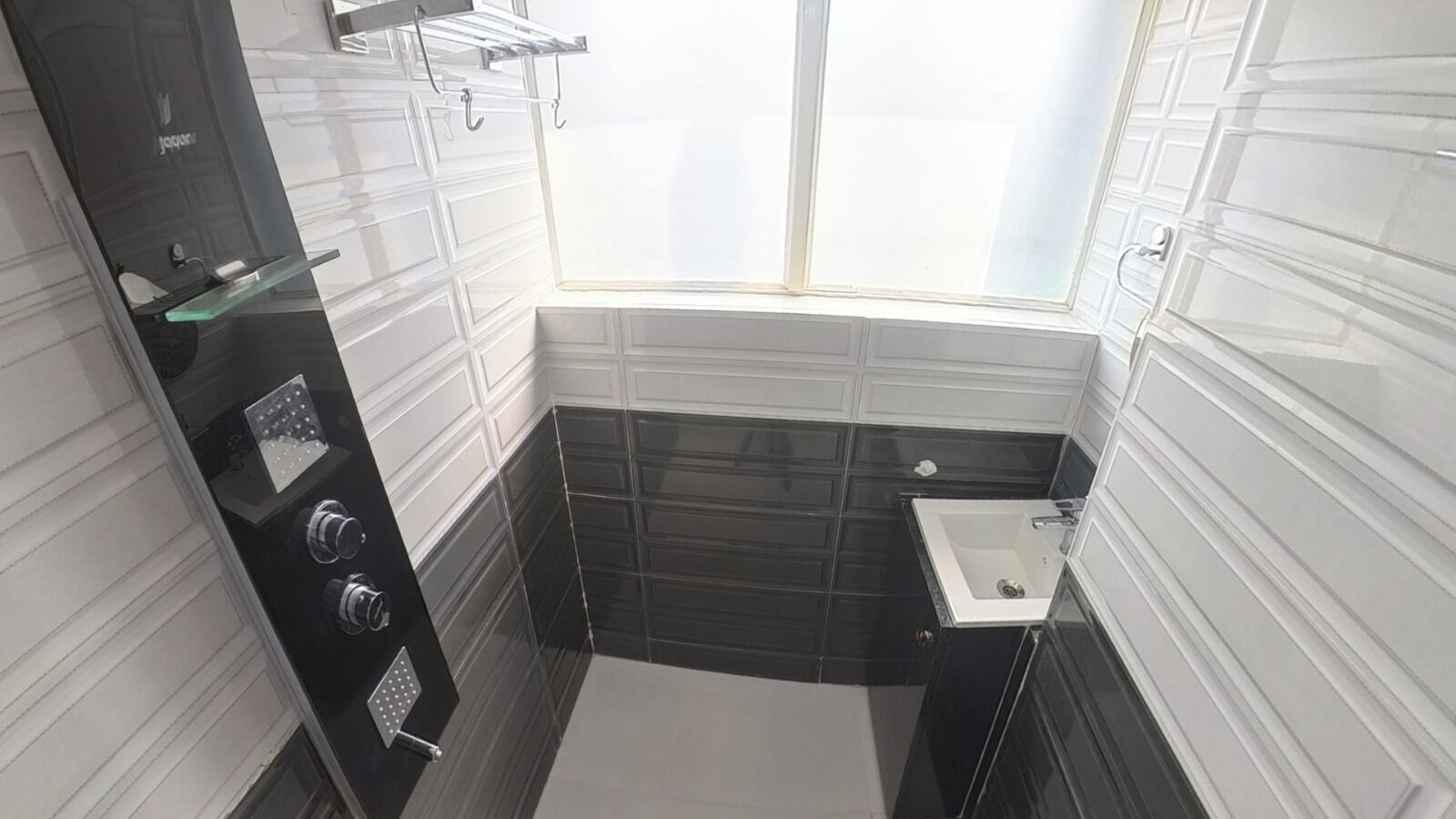 A small bathroom with a window, a sink, and a shower with controls.