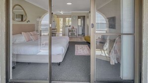 A hotel room with a bed, a desk, a chair, a mirror, and a view of the outside. - Beachside Studio Steps from Casey’s Beach (Batehaven)