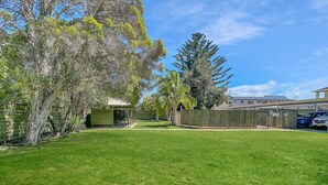 A well-maintained grassy yard with a wooden fence, a covered picnic area, and a tall tree. - Beachside Studio Steps from Casey’s Beach (Batehaven)