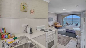A modern kitchen with a built-in stove, a sink, and a dining area with a view of the sea. - Beachside Studio Steps from Casey’s Beach (Batehaven)