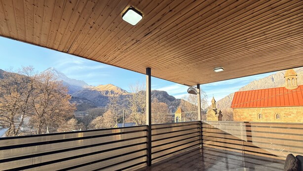 Una habitación moderna con techo de madera, barandilla de cristal y vistas a montañas e iglesia.
