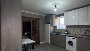 Una cocina compacta con lavadora integrada, una zona de comedor con mesa y sillas, y una puerta que da a una habitación oscura.