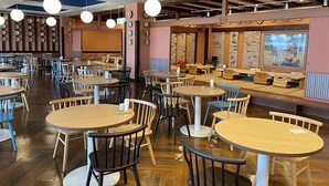 A spacious restaurant with round tables and chairs, a high ceiling with hanging lights, and a brick wall with a mural. - tabiyadoyobuko (Karatsu)