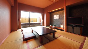 A traditional Japanese room with tatami flooring, a low table, chairs, a television, and a sliding door leading to a balcony. - tabiyadoyobuko (Karatsu)