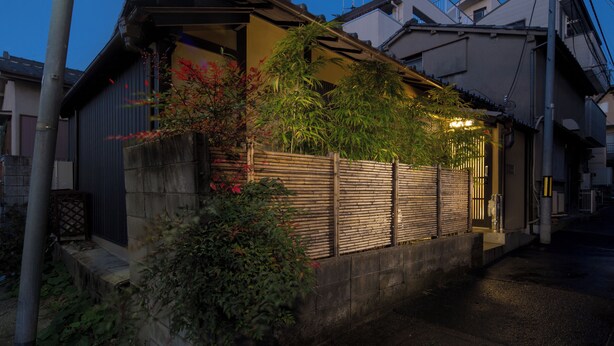 Ein traditionelles japanisches Haus mit Holzzaun, kleinem Garten und Blick auf die Straße.