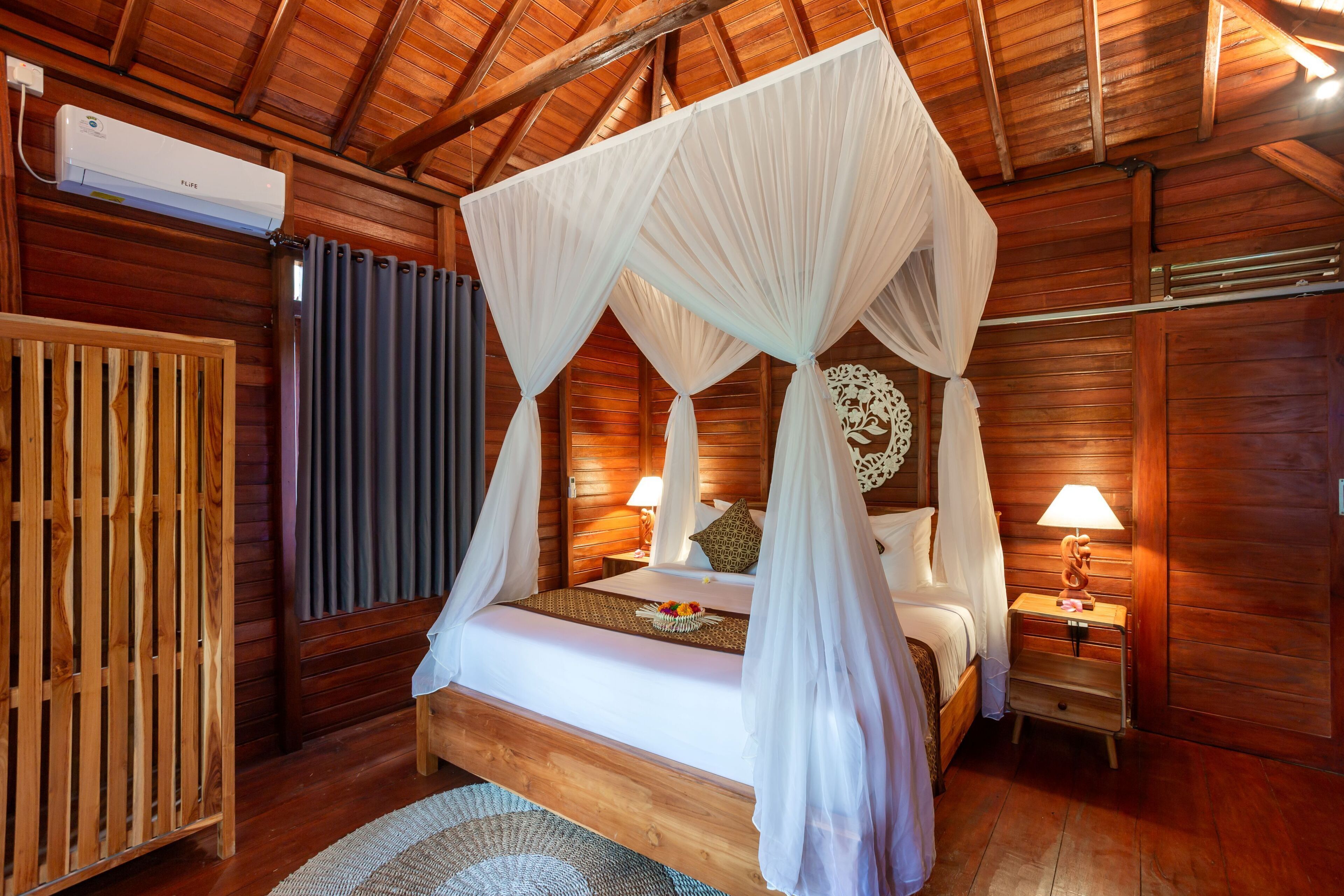 A wooden cabin-style bedroom with a four-poster bed, a nightstand with a lamp, and a wooden wardrobe.