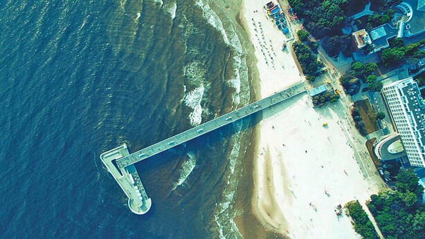 Vue aérienne d’une zone côtière avec un pont, une plage et des bâtiments adjacents.