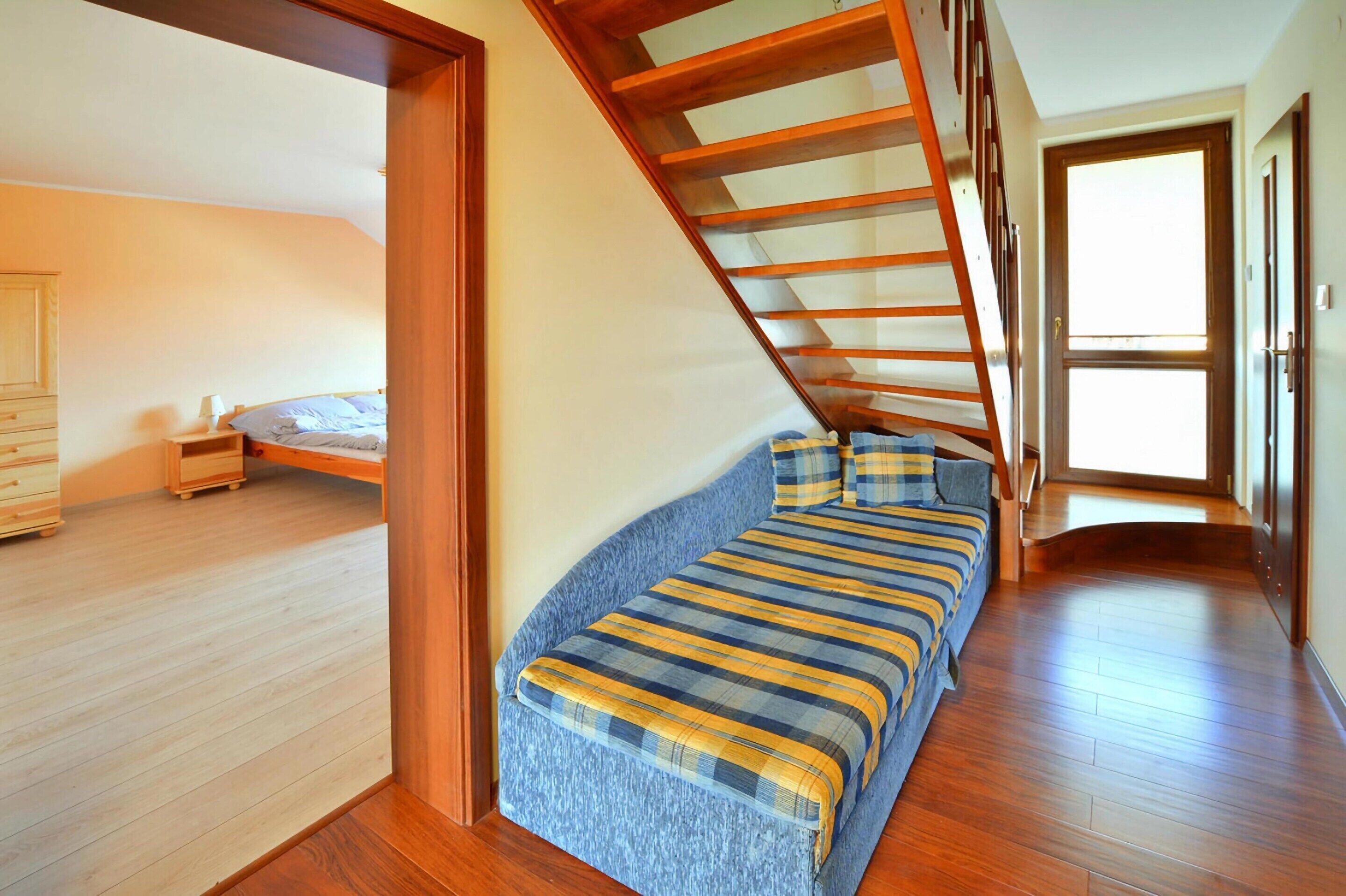 A bedroom with a loft bed, wooden flooring, and a staircase.