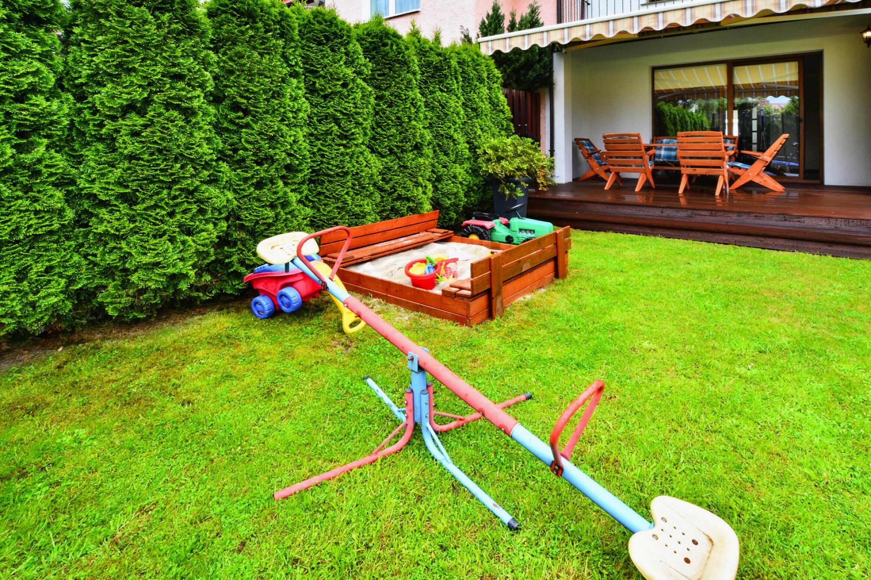 A well-maintained garden with a wooden playset, a bench, and a dining area with outdoor furniture.