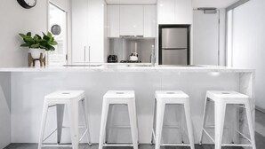 Une cuisine moderne avec des meubles blancs, un réfrigérateur en acier inoxydable et un coin bar avec des tabourets.