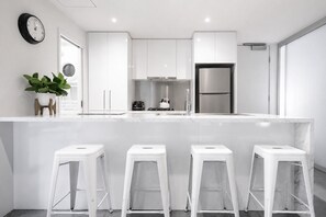 Eine moderne Küche mit weißen Schränken, einem Edelstahlkühlschrank und einer Bar mit Sitzgelegenheiten.