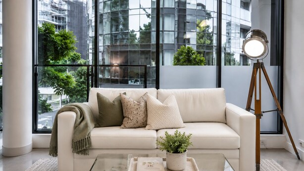 Un salon moderne avec un canapé blanc, une table basse en verre et un lampadaire sur trépied.