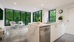 Une cuisine moderne dotée de grandes fenêtres, d’un lave-vaisselle et d’un coin salon agrémenté d’une plante.