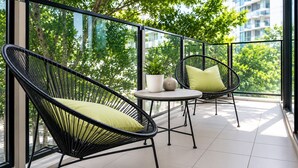 Un balcon avec deux fauteuils en osier, une petite table et une plante en pot.