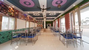 A spacious dining area with multiple tables and chairs, ceiling fans, and large windows providing natural light. - Deepak Resort (Chatabar)