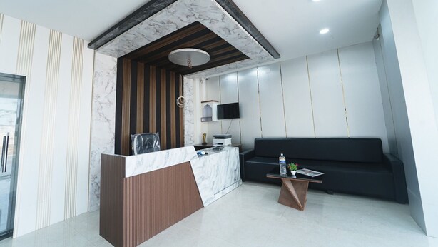 A modern reception area with a marble counter, a wooden accent wall, a black sofa, and a small table with a water bottle and magazine. - Deepak Resort (Chatabar)