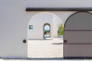 Une entrée d’immeuble avec un chemin de gravier, une porte en arc de cercle et un grand portail en métal.
