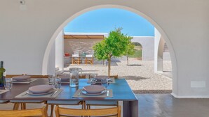 Un'area pranzo con un tavolo apparecchiato per quattro persone, un piccolo albero e una vista attraverso un arco.