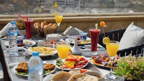 A table with various breakfast items, including bread, eggs, and a fruit salad, set on a balcony with a city view. - eco home suite (Giza)