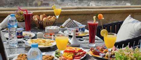 Une table dressée sur un balcon avec vue sur la ville, où sont disposés divers aliments pour le petit-déjeuner, notamment du pain, des œufs et une salade de fruits.