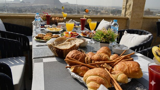 A table set with food and drinks, overlooking a cityscape with pyramids. - eco home suite (Giza)