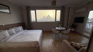 A hotel room with a bed, a small round table with chairs, a TV, and a view of a mountain. - eco home suite (Giza)