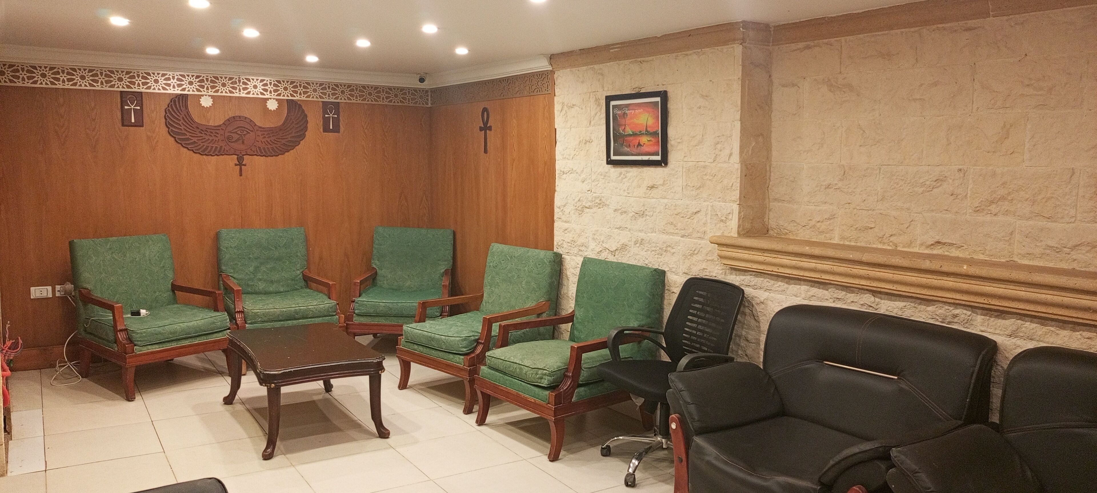 A room with six green cushioned chairs, a wooden coffee table, and a black office chair.