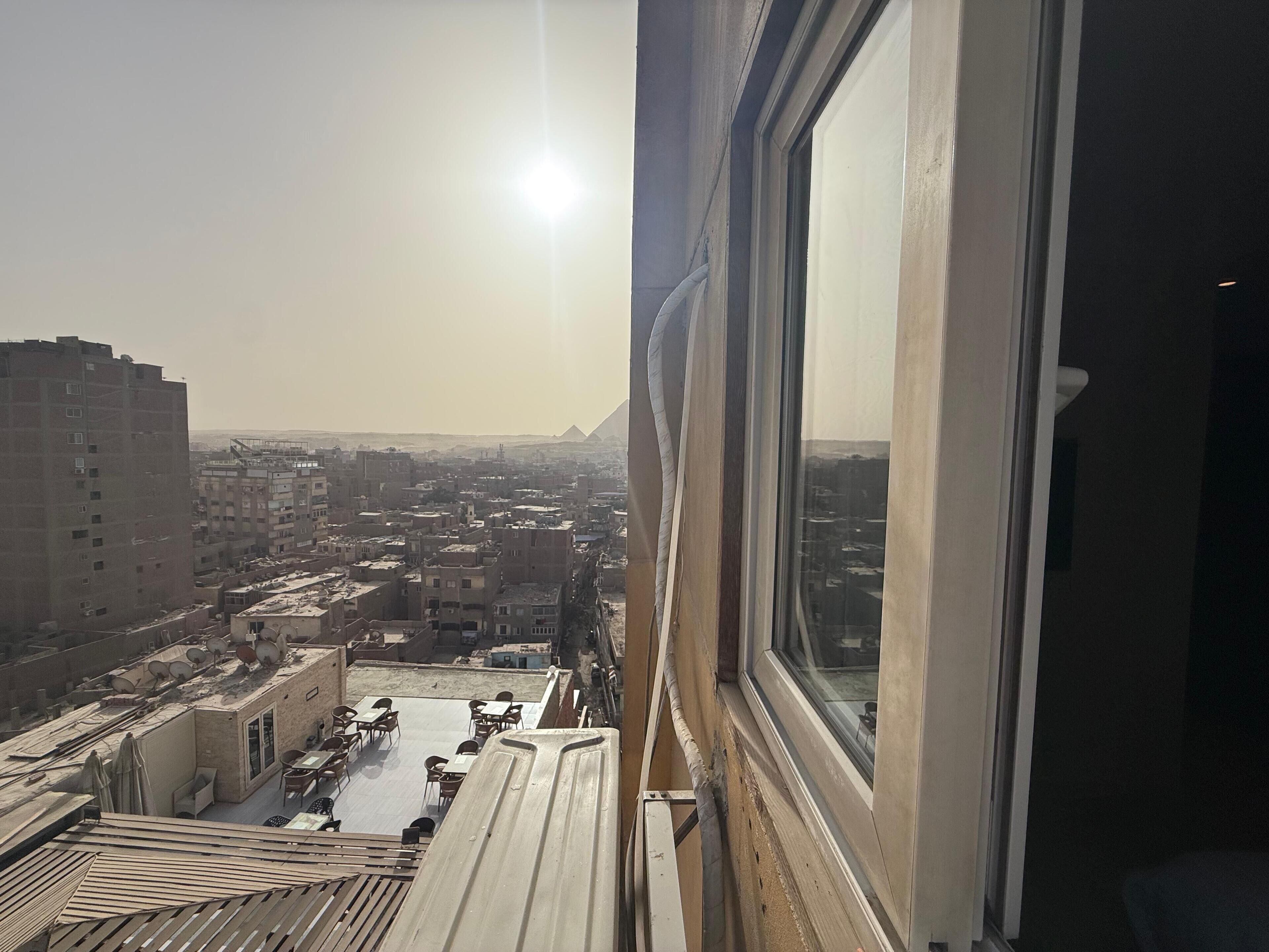 Vista desde una ventana sobre un paisaje urbano con edificios y una pirámide a lo lejos.