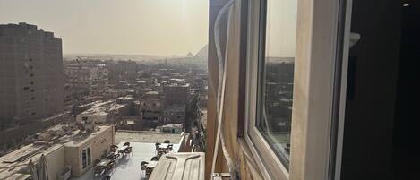 Vista desde una ventana sobre un paisaje urbano con edificios y una pirámide a lo lejos.
