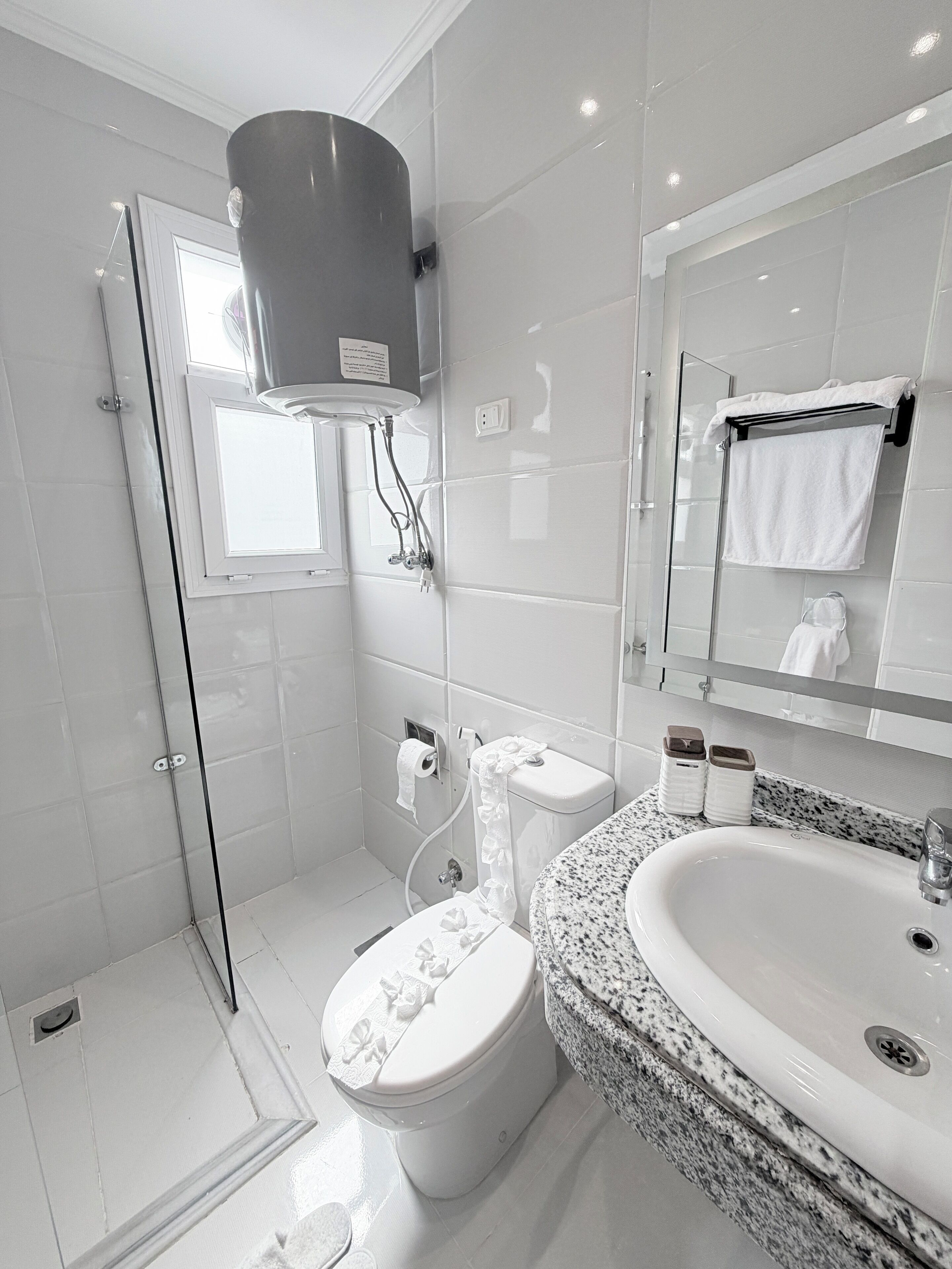 Un baño moderno con cabina de ducha de vidrio, un inodoro con tapa decorativa, un lavabo con encimera de granito y un espejo sobre el lavabo.