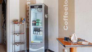 A vending machine with a Coca-Cola logo, a refrigerator with shelves, and a table with a teapot and menu. - Room "Room 1" in Extertal (Extertal)