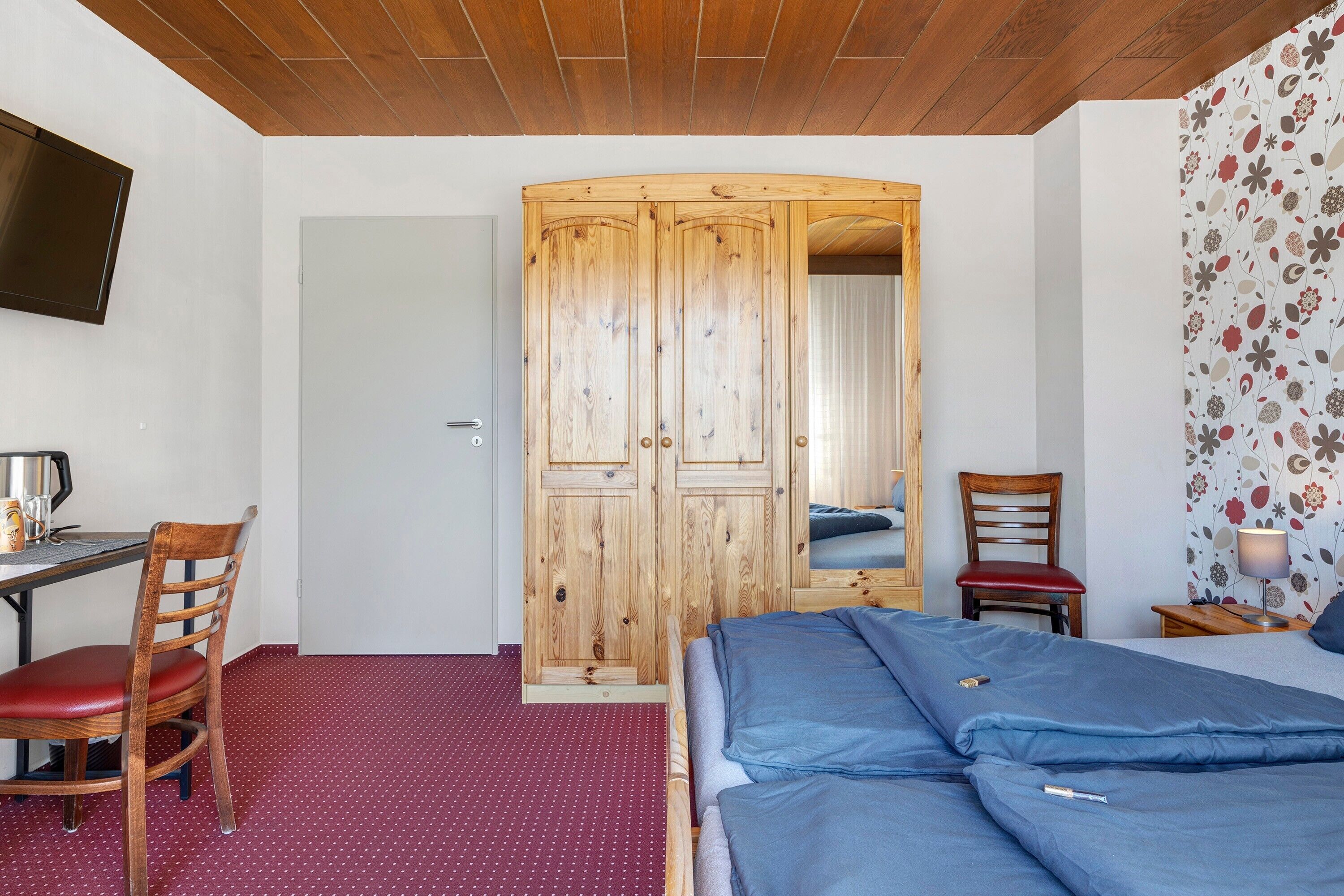 Ein Zimmer mit Bett, Schreibtisch, Stuhl, Kleiderschrank und Fernseher an der Wand.