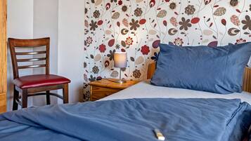 Ein Schlafzimmer mit einem Bett, einem Sessel, einem Nachttisch mit Lampe und einer Wand mit Blumenmuster.