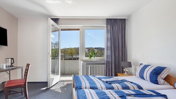 A hotel room with a bed, a chair, a desk, a TV, a window with curtains, and a view of trees. - Room "Room 2" with Balcony (Extertal)