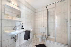 Un baño con lavamanos blanco, espejo, inodoro y ducha.