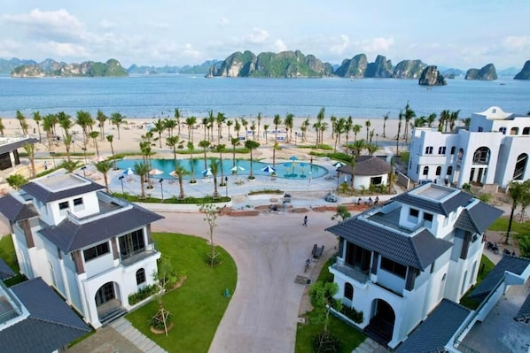 A resort with a central pool, surrounded by palm trees and beachfront views.