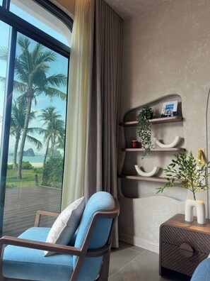 Une chambre moderne avec une grande fenêtre, une chaise en bois, une table d’appoint avec un vase et une étagère murale ornée d’objets décoratifs.