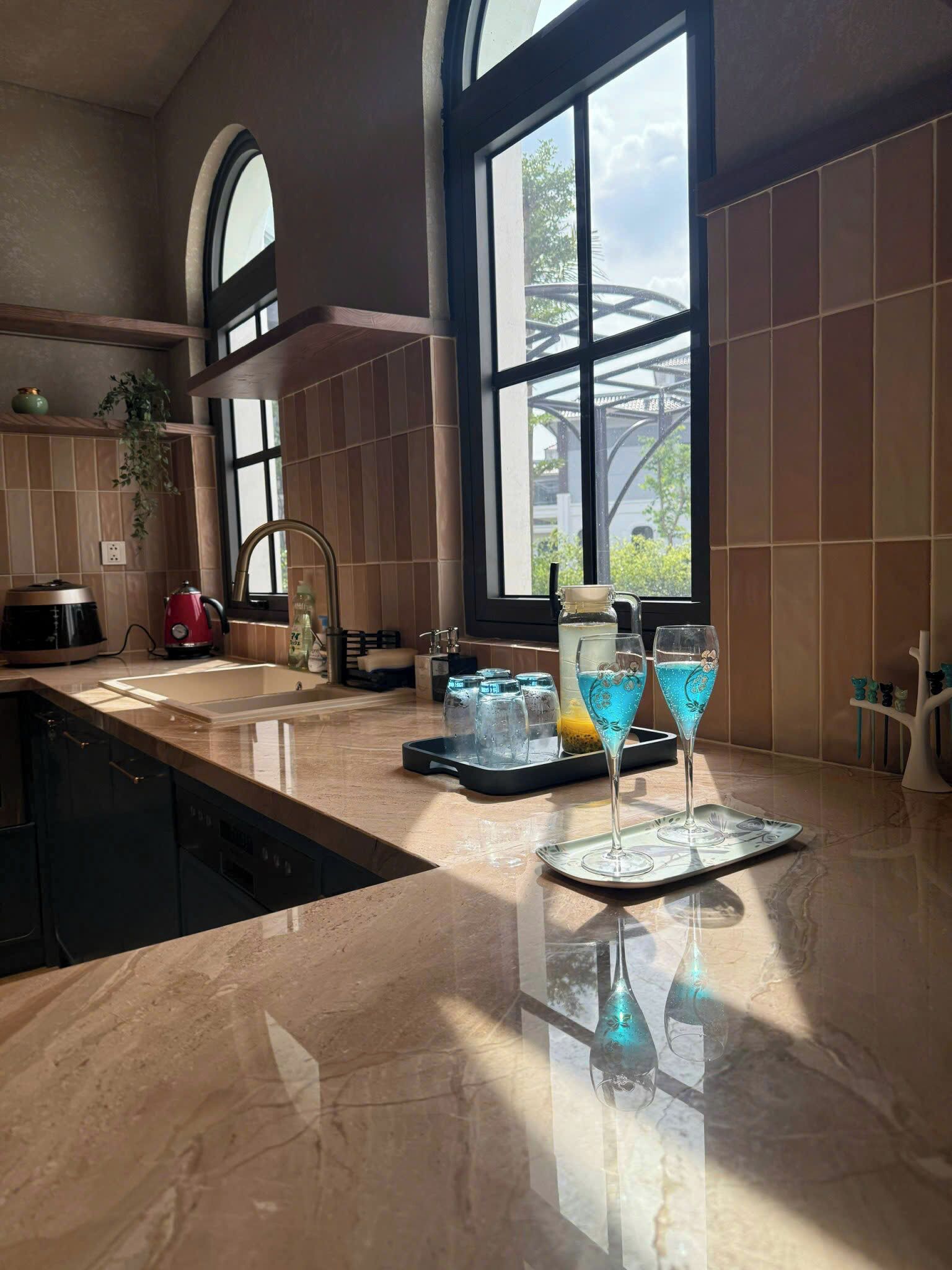 A kitchen with a large window, a sink, a coffee maker, and a tray with glasses.