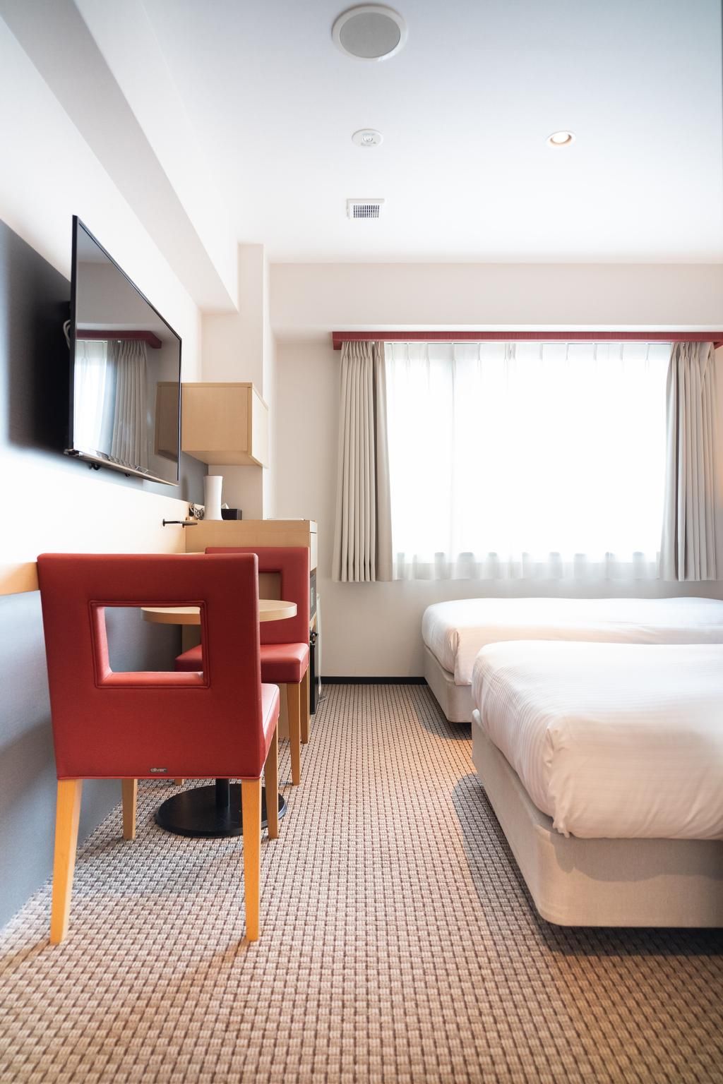 Habitación de hotel con una cama, un escritorio con silla, un televisor y una ventana con cortinas.