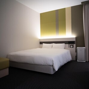 Une chambre d’hôtel avec un lit, une table de chevet, une lampe, une horloge et un radiateur.