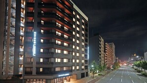 Een hotel met meerdere verdiepingen, verlichte ramen en balkons, een nette straat ervoor en een heldere nachthemel.